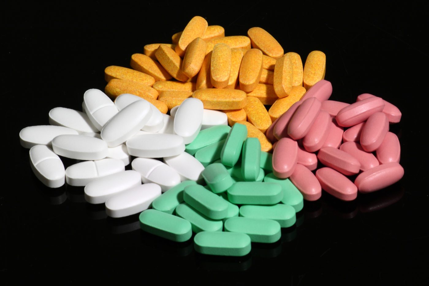Comprimidos farmacêuticos de diferentes cores e formatos sobre fundo escuro